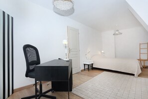 Ein Schlafzimmer mit einem Bett, einem Schreibtisch mit Stuhl, einem kleinen Nachttisch, einer Pendelleuchte und einer Tür.