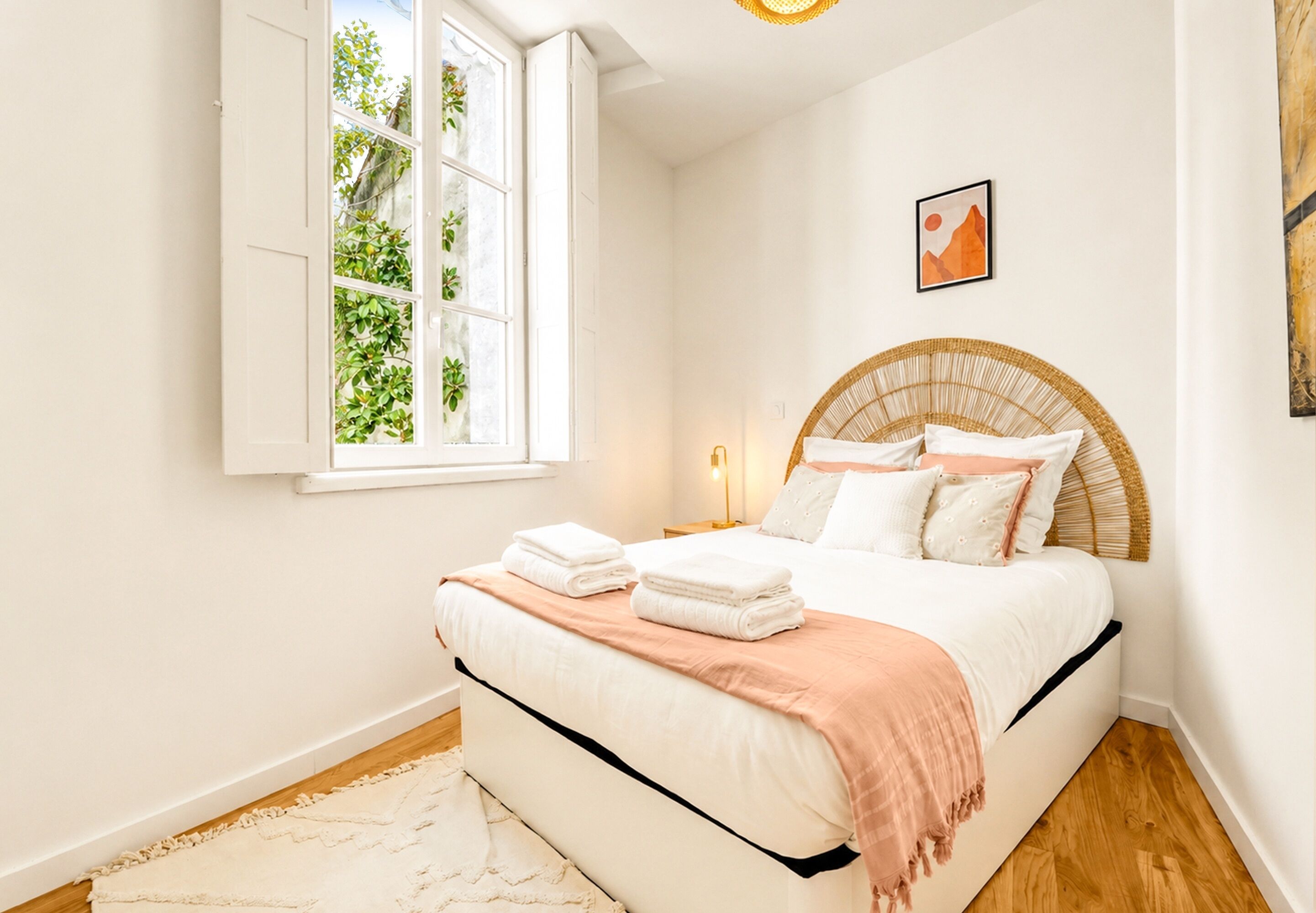 Un dormitorio con cama, ventana, mesita de noche y una obra de arte colgada en la pared.