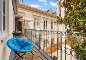 A balcony with a blue chair, a wooden table, and a view of neighboring buildings. - La Fabrik Matabiau - Charmant appt avec terrasse et parking (Toulouse)