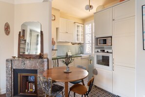 A compact kitchen with white cabinets, a built-in microwave, and a dining area with a round table and chairs. - Le Flamand - Appt de charme au centre de Rennes (Rennes)