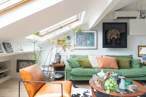 Un salon moderne doté d’un plafond en pente, d’un canapé vert, d’un fauteuil en cuir et de divers objets décoratifs.