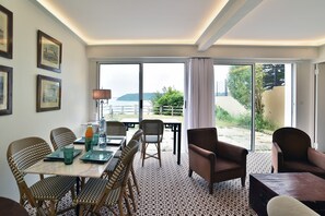 A dining area with wicker chairs, a table with a glass top, and a view of the outdoors. - L'Aiguillon - À 500 m de la plage (Saint-Cast-le-Guildo)