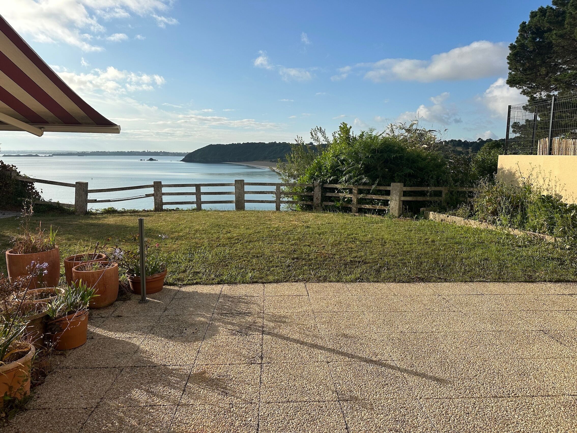 A gravel patio with potted plants, a wooden fence, and a view of the sea.