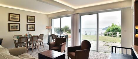 A spacious living area with a sofa, armchairs, a coffee table, a dining table with chairs, and a large window offering a view of the outdoors.