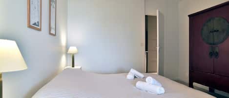 A hotel room with a large bed, a wooden wardrobe, and two framed pictures on the wall.