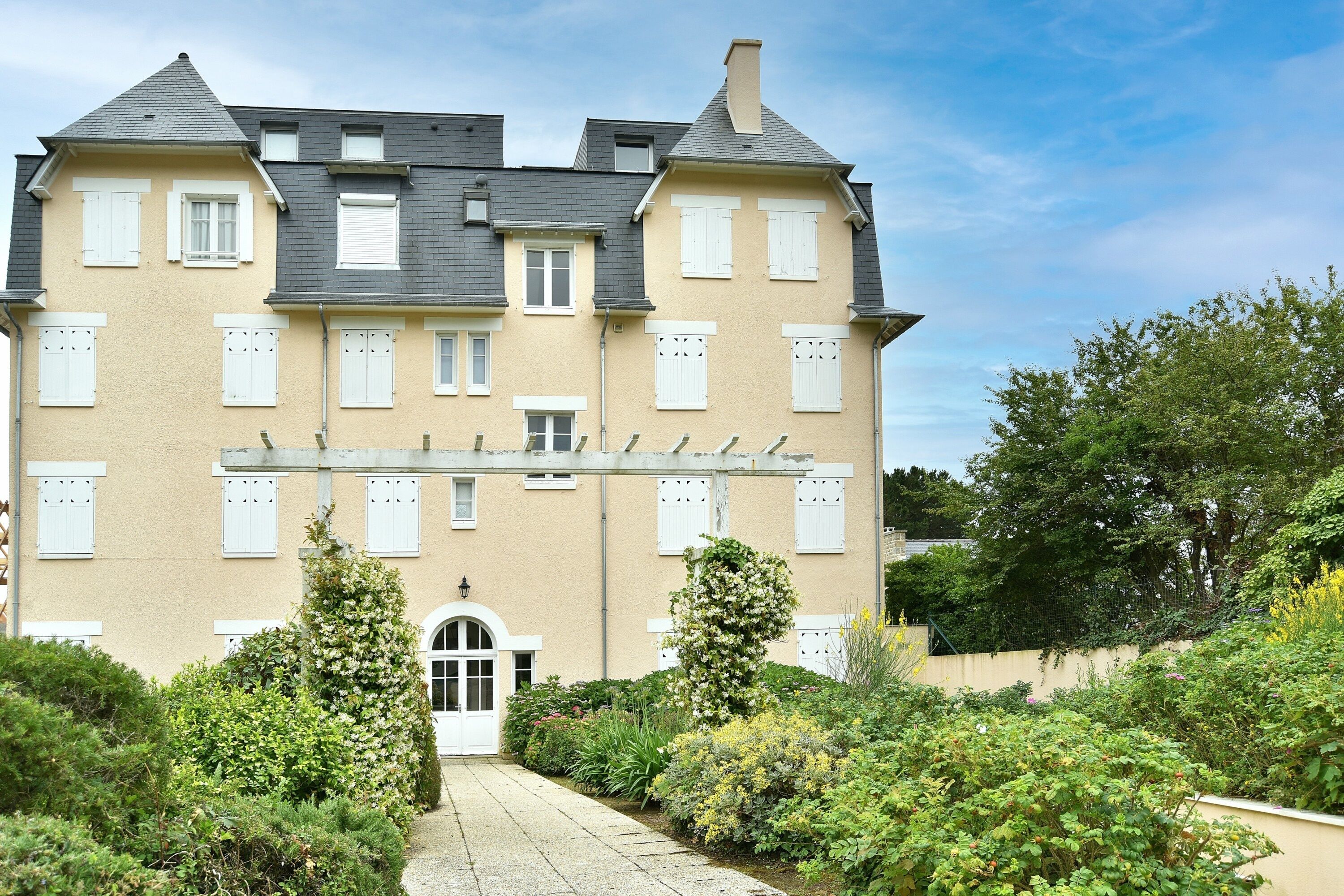 A large, two-story building with a symmetrical facade, multiple windows with shutters, and a central entrance.