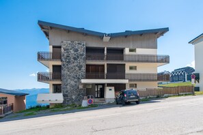 A multi-story building with balconies, a stone facade, and a car parked in front. - Le Refuge de Saint-Lary - 500m station de ski (Saint Lary-Soulan)