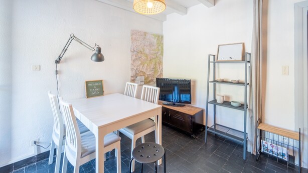 A dining area with a table, chairs, a lamp, a television, and a shelf with bowls. - Le Refuge de Saint-Lary - 500m station de ski (Saint Lary-Soulan)