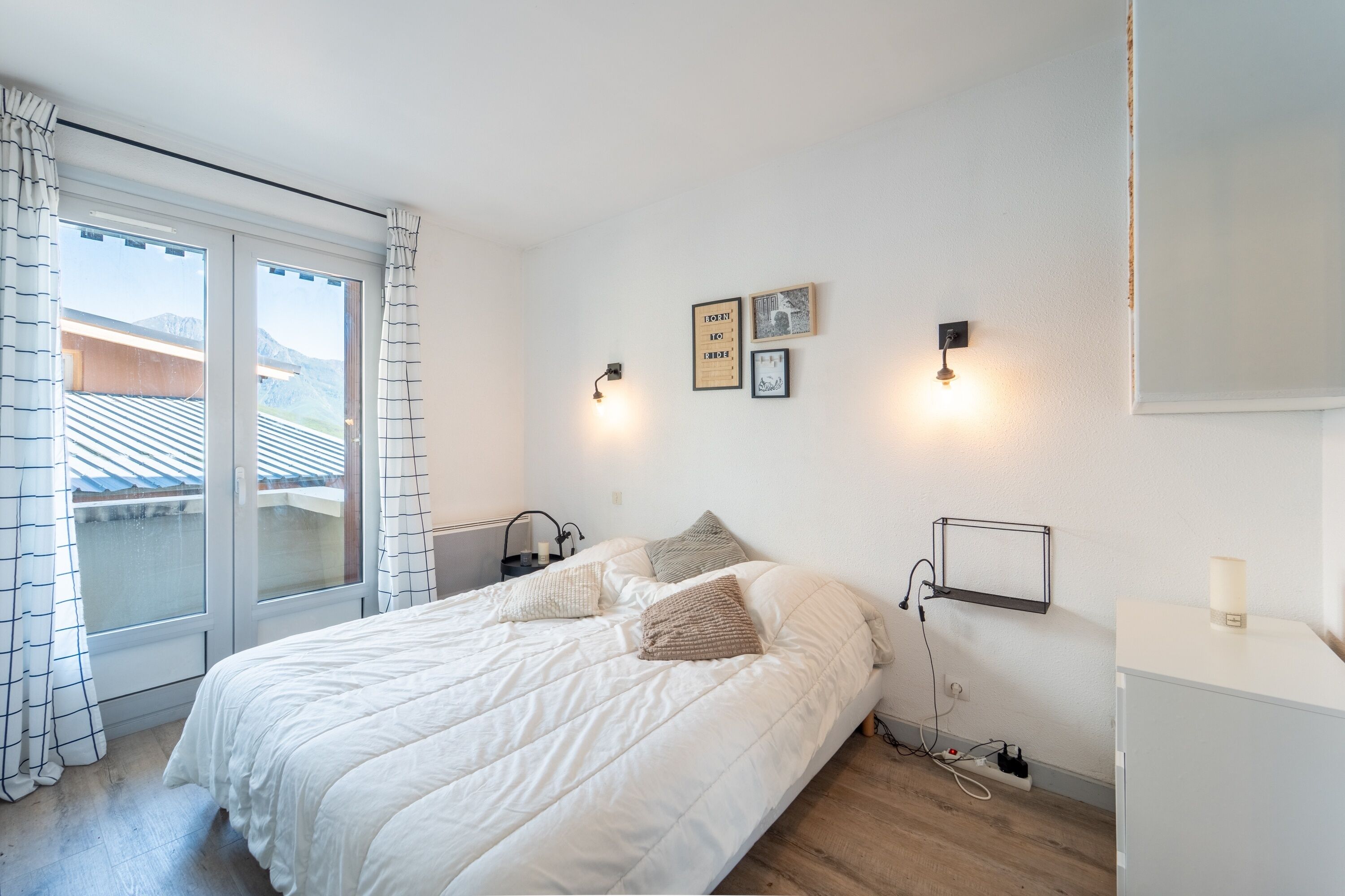 Une chambre à coucher comprenant un lit, une table de chevet, une étagère fixée au mur et une fenêtre avec des rideaux.