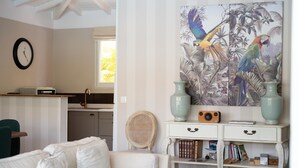 Um quarto com um sofá branco, uma estante com livros, um rádio e um quadro de pássaros na parede.