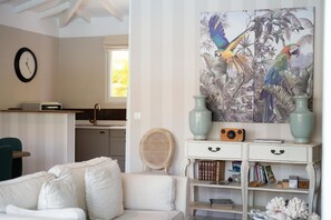 Ein Zimmer mit einem weißen Sofa, einem Bücherregal voller Bücher, einem Radio und einem Vogelbild an der Wand.