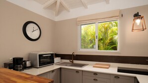 Uma cozinha com um relógio, uma janela com vista para vegetação e uma cafeteira.