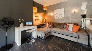 Ein modernes Wohnzimmer mit grauem Sofa, einem weißen Schreibtisch und einem schwarzen Ventilator.