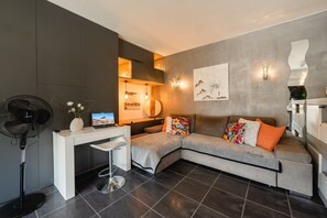 Ein modernes Wohnzimmer mit grauem Sofa, einem weißen Schreibtisch und einem schwarzen Ventilator.
