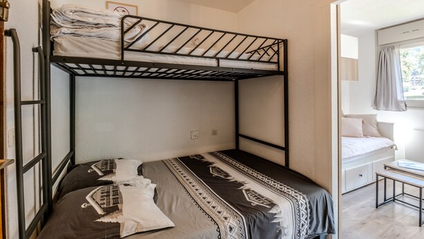 Ein Schlafraum mit Etagenbett, Fenster, Schreibtisch und einem Bett mit gemusterten Bettbezügen.