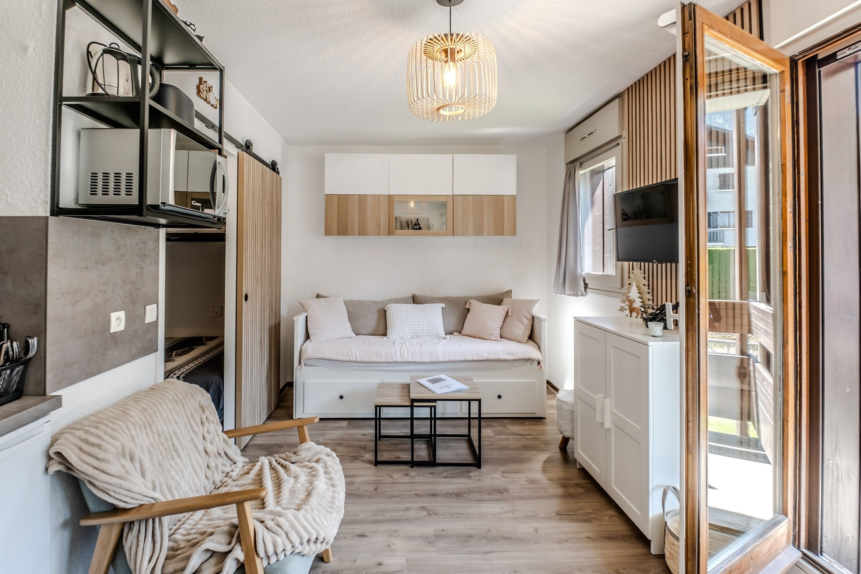 Un espace de vie compact comprenant un lit, une petite table, une chaise, un coin cuisine intégré et une grande fenêtre.