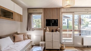 Ein modernes Wohnzimmer mit einer Couch, einem Flachbildfernseher, einem kleinen Tisch und Blick ins Freie.