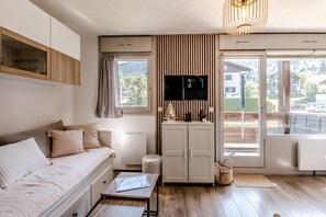 A modern living room with a sofa, a flat-screen TV, a small table, and a view of the outside. - Le Cocon Montagnard - Studio avec balcon & parking (Arâches-la-Frasse)