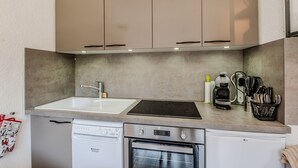 Eine kompakte Küche mit Geschirrspüler, Backofen und Kaffeemaschine auf der Arbeitsplatte.
