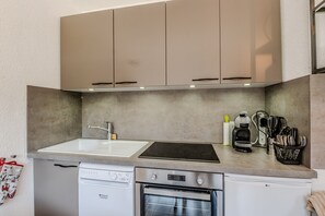 A compact kitchen with a dishwasher, oven, and a coffee maker on the countertop. - Le Cocon Montagnard - Studio avec balcon & parking (Arâches-la-Frasse)