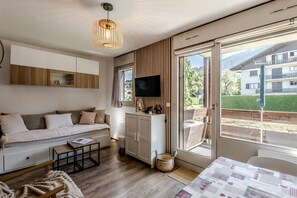 A modern living room with a sofa, coffee table, and a television. - Le Cocon Montagnard - Studio avec balcon & parking (Arâches-la-Frasse)
