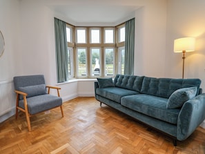 A room with a corner bay window, a grey armchair, a blue sofa, and a floor lamp.