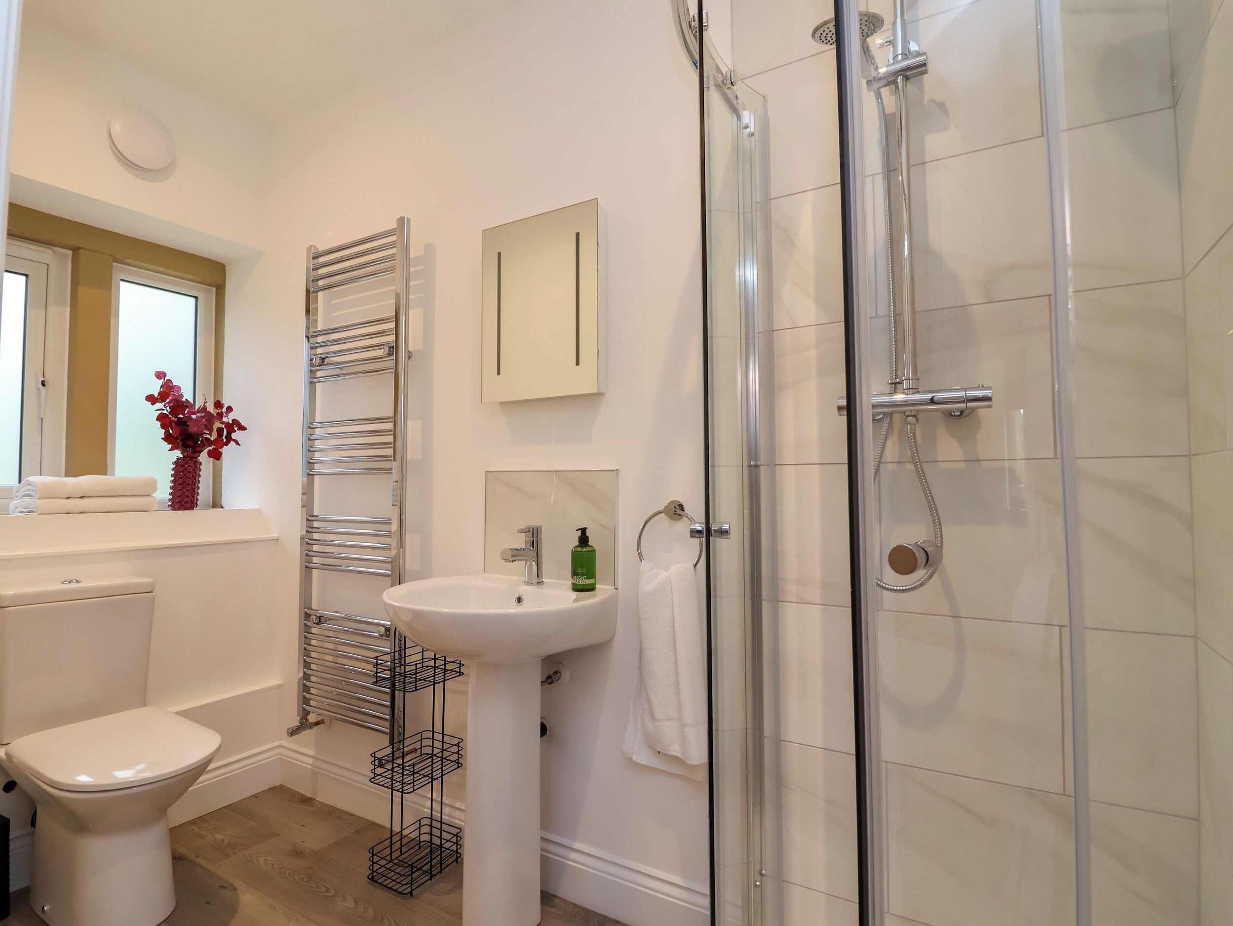 A modern bathroom with a toilet, sink, shower, and towel rack.