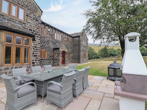 Un bâtiment en pierre doté d’un patio aménagé avec des meubles en osier et un barbecue.