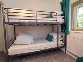 Una cama litera con ropa blanca y una almohada verde, un radiador y una ventana con cortinas.