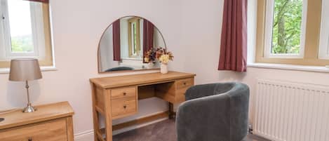 Une chambre à coucher avec un bureau en bois, une chaise, un miroir, une commode et une fenêtre avec des rideaux.