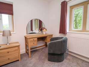 Une chambre à coucher avec un bureau en bois, une chaise, un miroir, une commode et une fenêtre avec des rideaux.