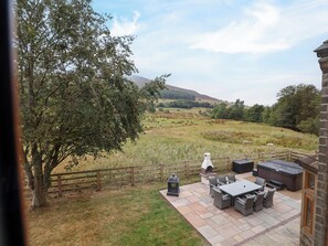 A patio with outdoor furniture, a grill, and a view of a grassy field with sheep.