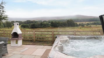 A hot tub and a wood-fired pizza oven on a patio with a view of a grassy field and hills.