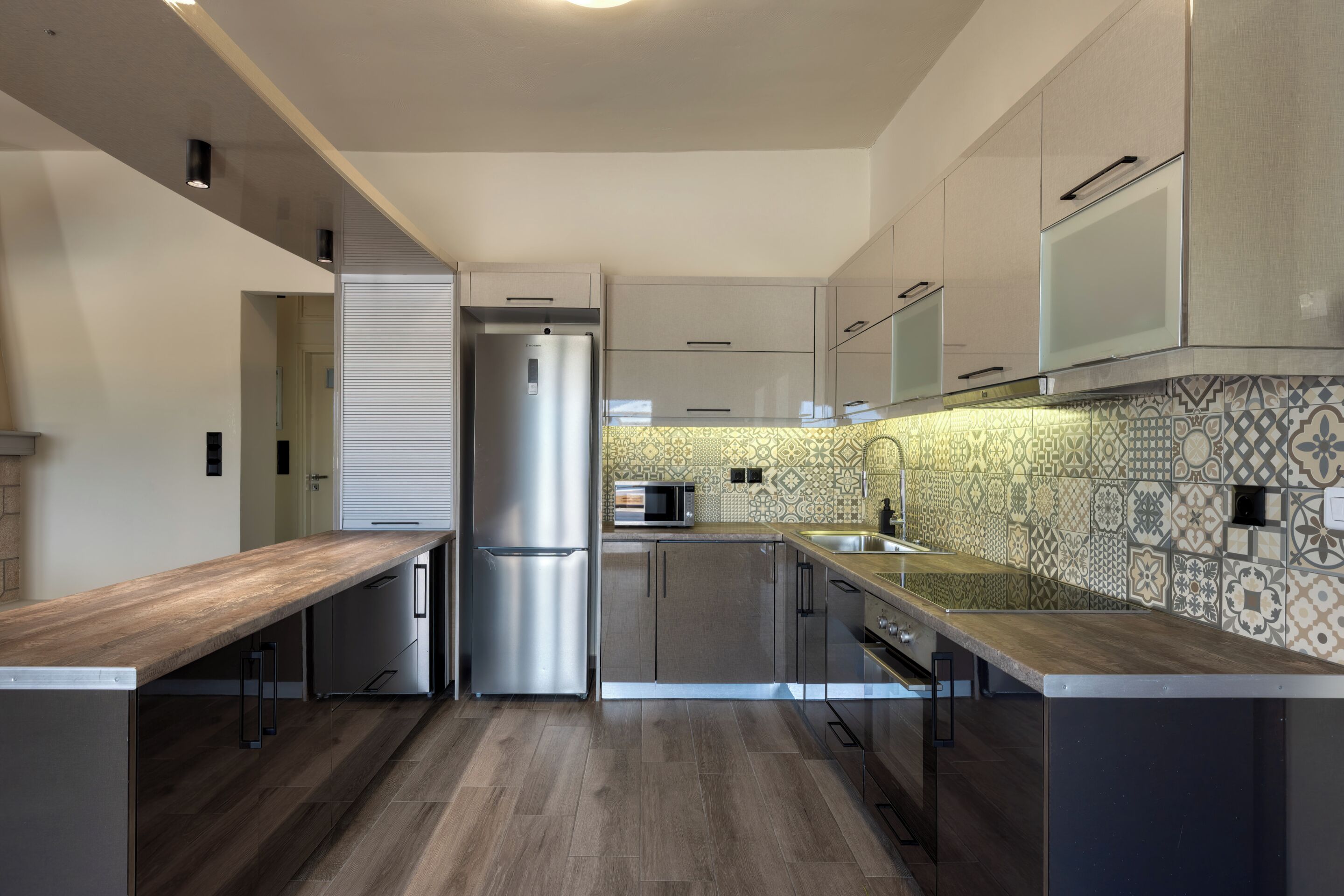 A modern kitchen with a wooden countertop, stainless steel appliances, and patterned backsplash.