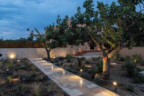 A garden pathway with trees, a stone wall, and a building in the background.