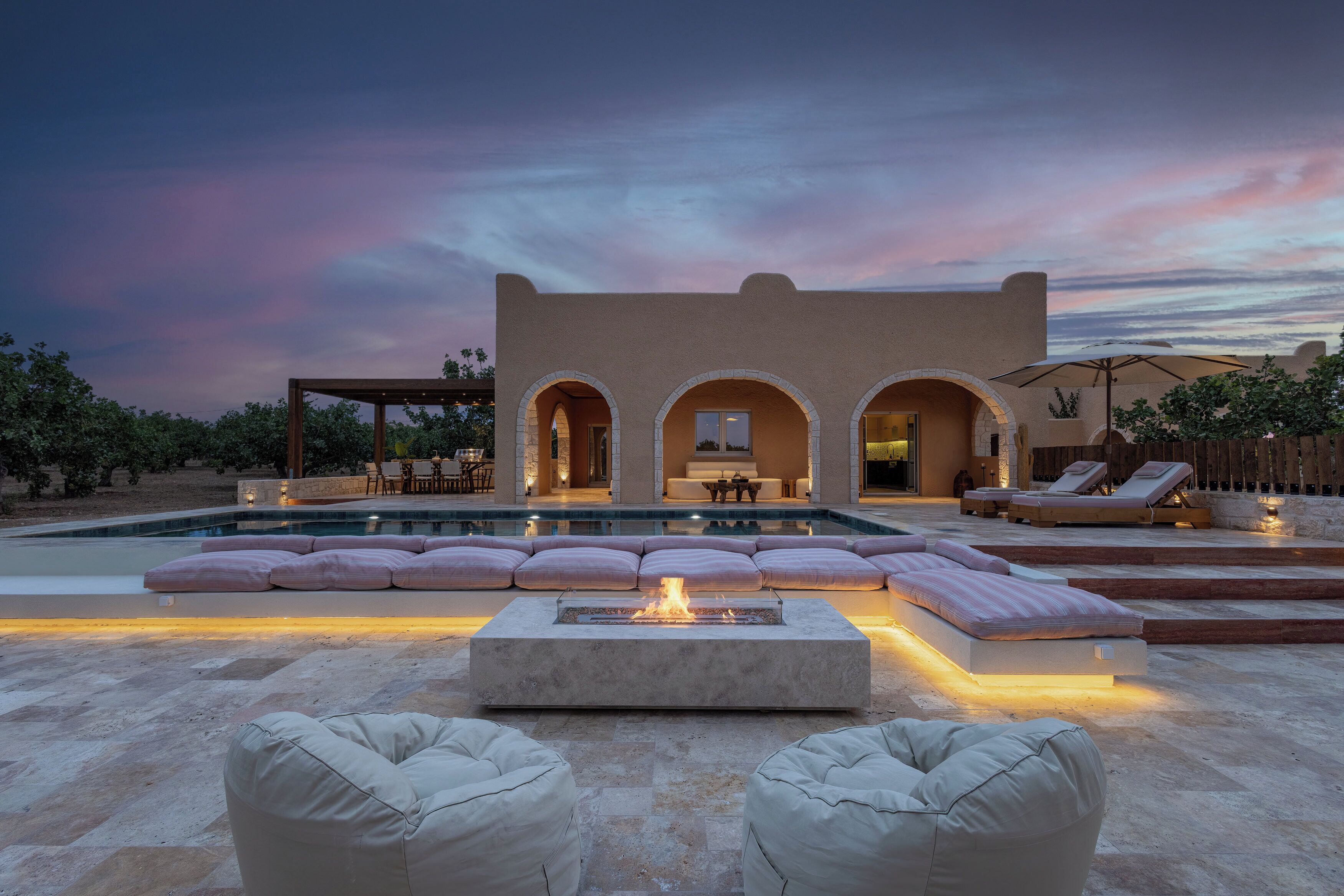 Una zona de piscina con una chimenea, asientos y un edificio con ventanas arqueadas.