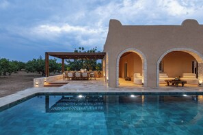 A poolside area with a pergola, outdoor seating, and a stone structure with arches.