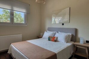 Ein Schlafzimmer mit einem Bett, Nachttischen, einem Heizkörper, einem Fenster mit Jalousien und einem Wandbild.