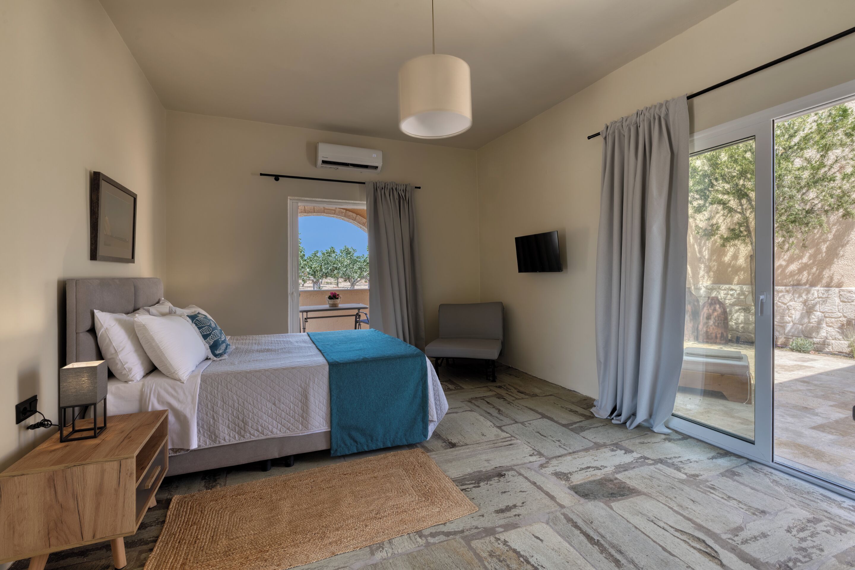 A bedroom with a bed, bedside table, lamp, and a view of the outdoors.