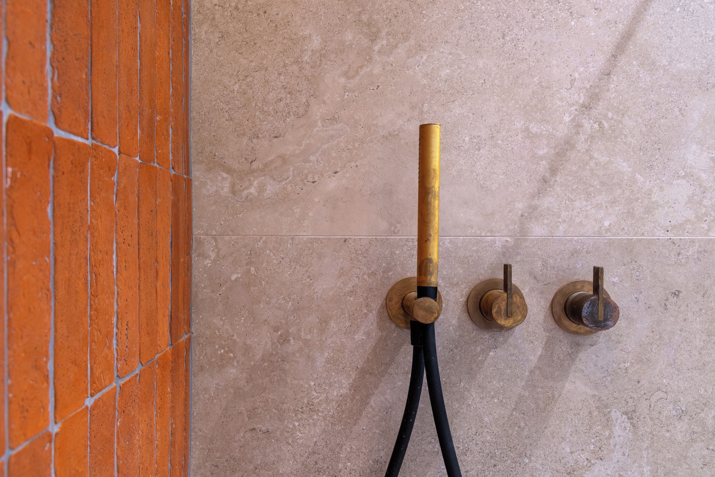 A shower with a gold-colored faucet and a black hose.