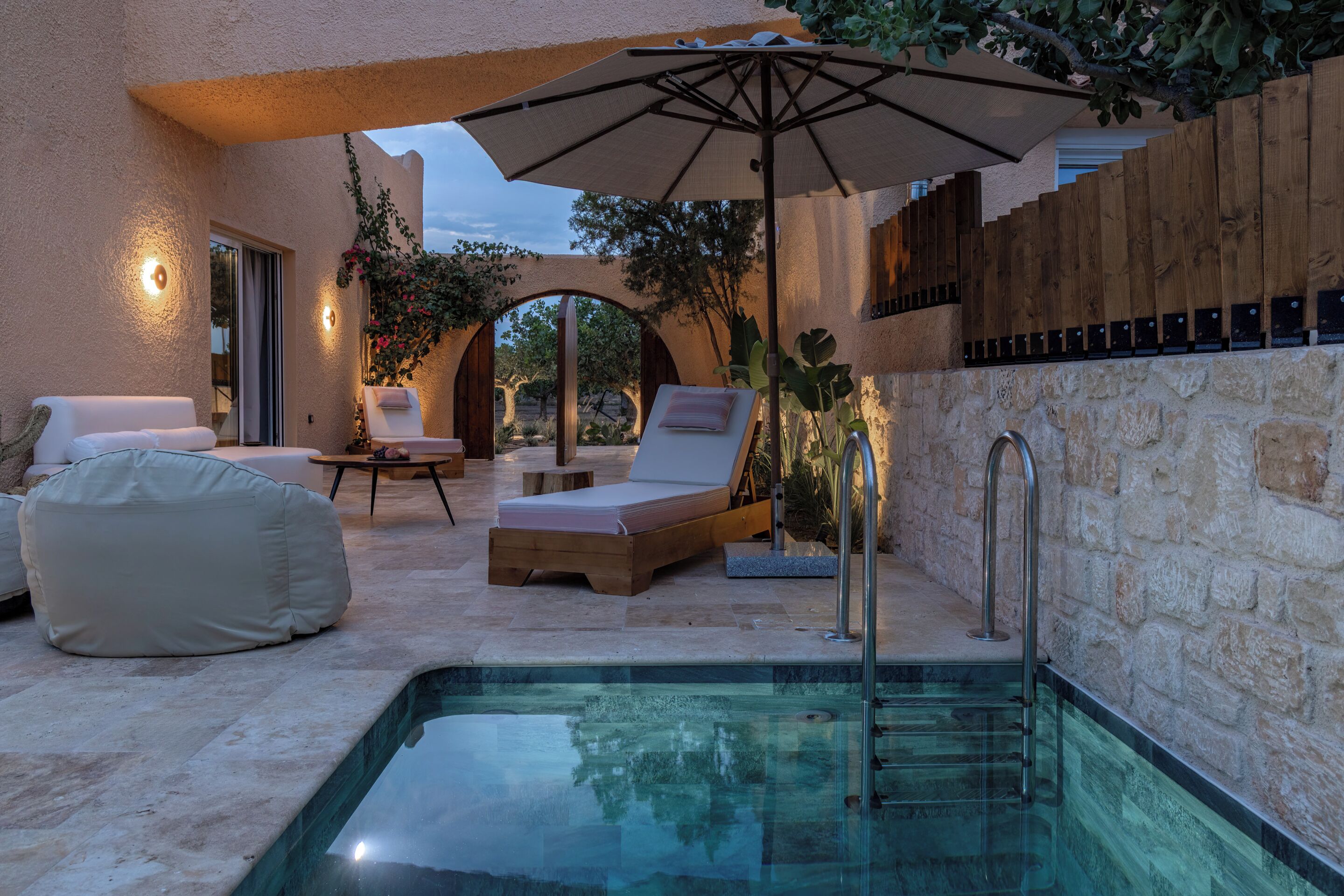 A poolside area with lounge chairs, a wooden deck, and a stone wall.
