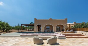 Ein moderner Poolbereich mit blauem Himmel, einem Pool mit rosa Kissen und einer Holzterrasse mit Liegestühlen.