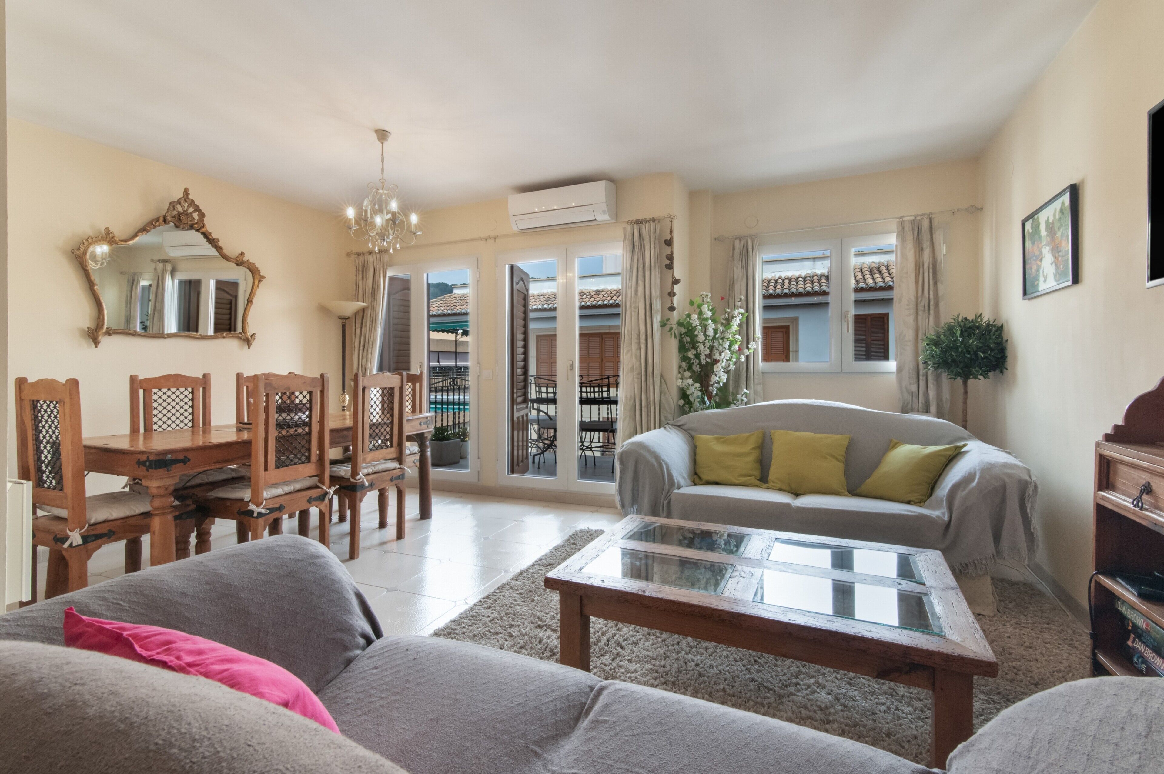 A living room with a sofa, a coffee table, a dining table with chairs, a chandelier, and a large mirror.