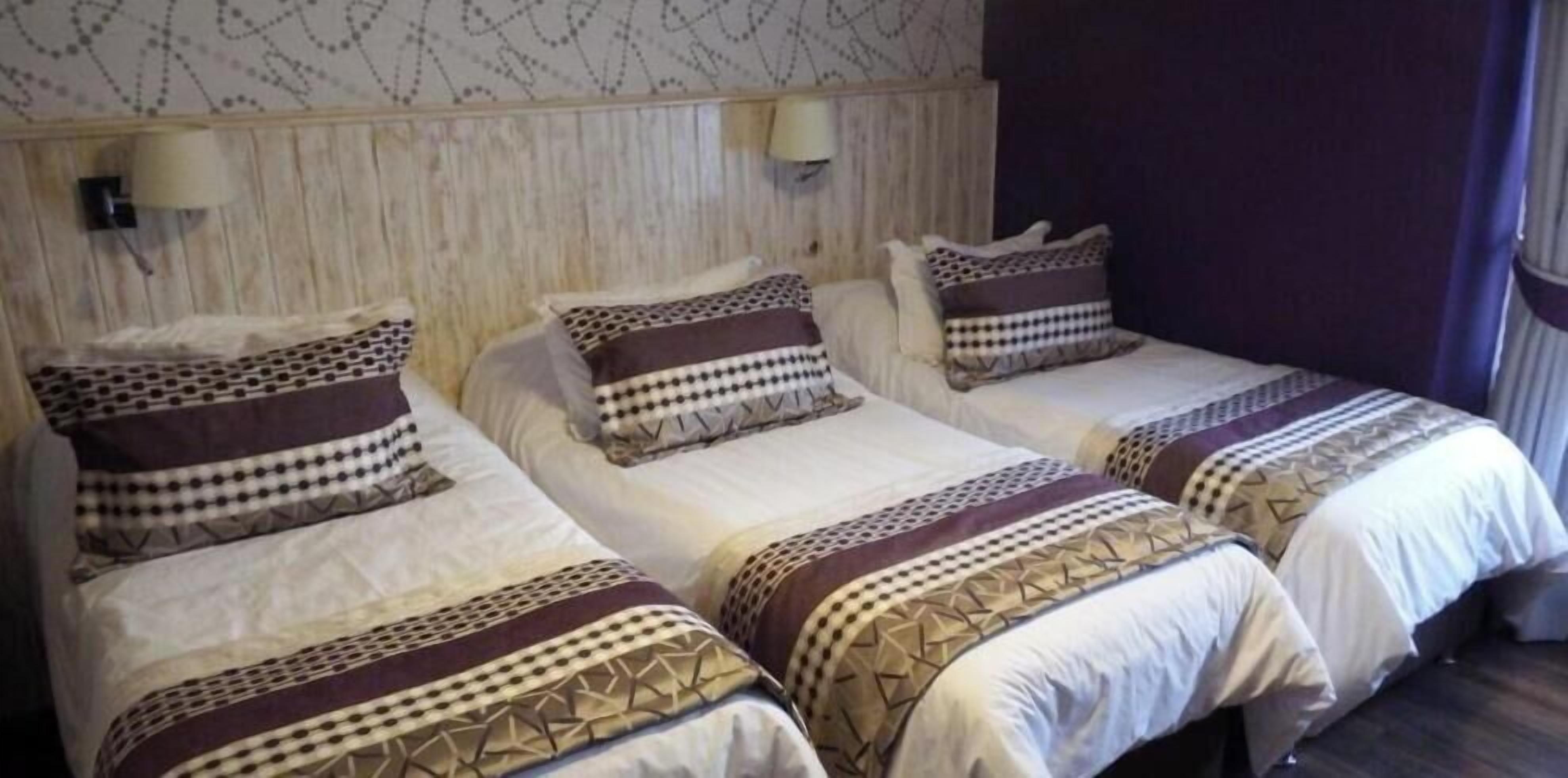 A hotel room with three beds, each with patterned bedding and headboards.