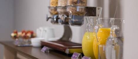 Una barra de desayuno con una máquina de café, una exhibición de frutas y un dispensador de agua.