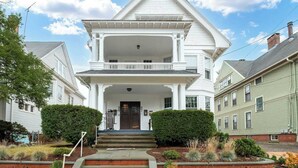 A two-story house with a front porch, a central door, and a small garden area with shrubs and plants. - Apt Near Yale|Walkable&Cozy/ for Connection & Rest (New Haven)