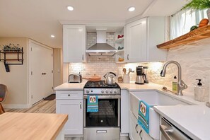 A modern kitchen with white cabinetry, a gas stove, a built-in oven, a coffee maker, and a sink with a faucet. - Enjoy a comfortable stay in New Haven, perfectly located near Yale and the city’s top attractions. This cozy home offers a peaceful neighborhood setting while keeping you just minutes from downtown dining, shopping, and cultural spots. (New Haven)