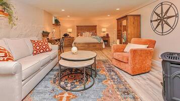 A cozy living room with a sofa, armchair, round table, and a bed with a headboard.