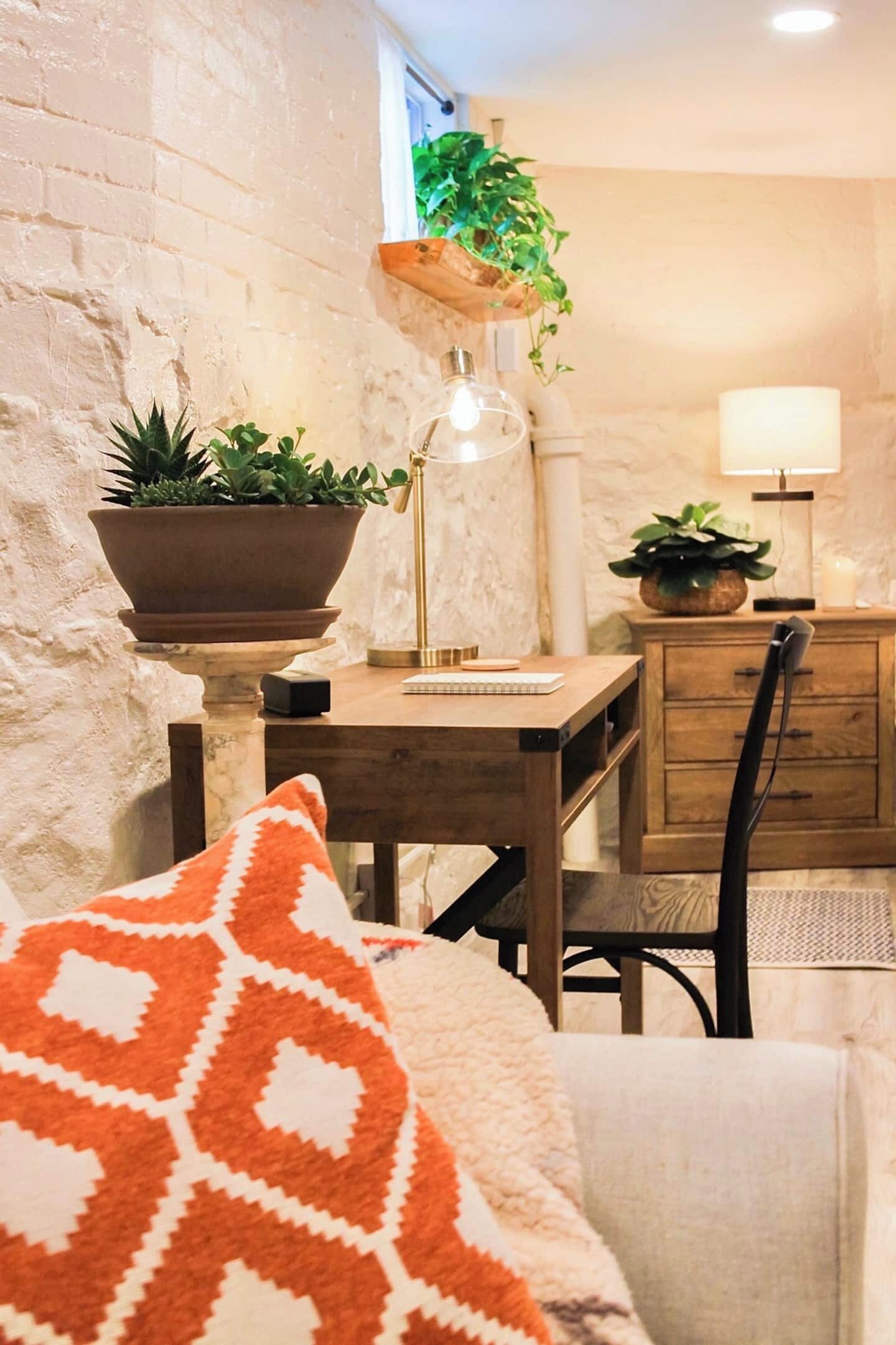 A cozy room with a wooden desk, a chair, a lamp, and a potted plant.
