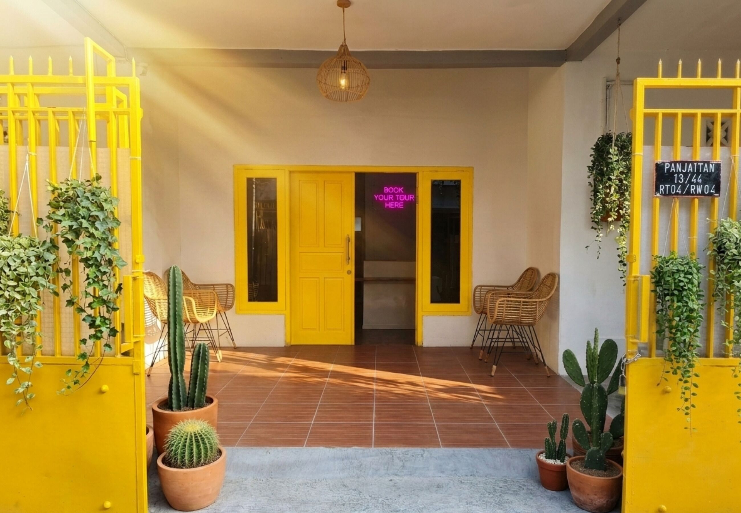 A yellow gate with a neon sign, a cactus plant, and a door with a neon sign.